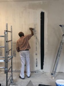 Léon qui pose de l'enduit sur un mur du salon de l'appartement pendant sa rénovation